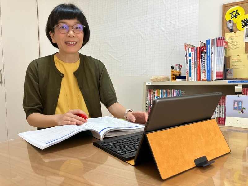 ハマヨビ事務局長 平井綾子が原稿用紙とタブレットを前に微笑む様子